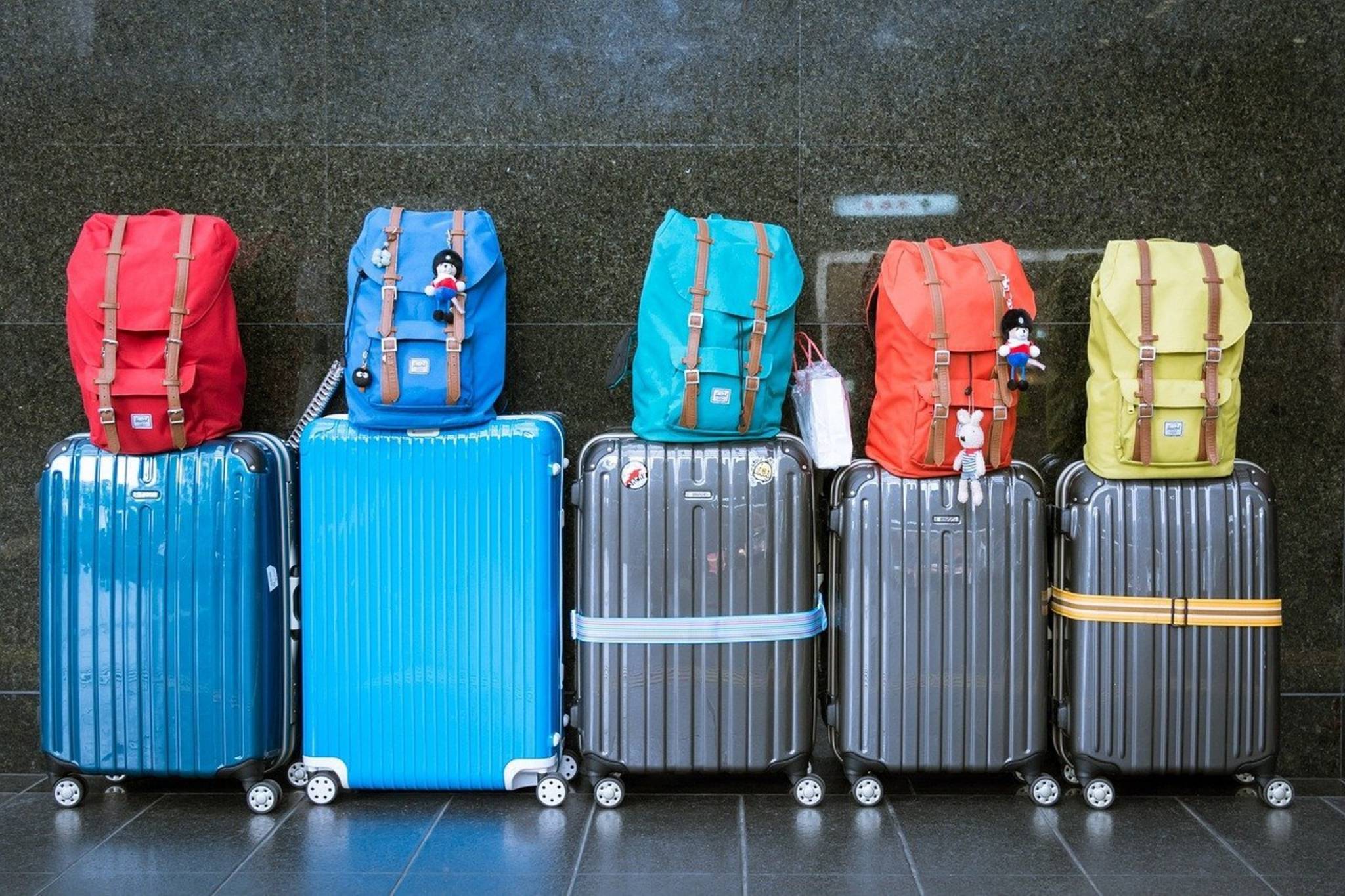 Fünf Reisekoffer mit je einem Rucksack obenauf stehen in einer Rehei nebeneinander vor einer Wand